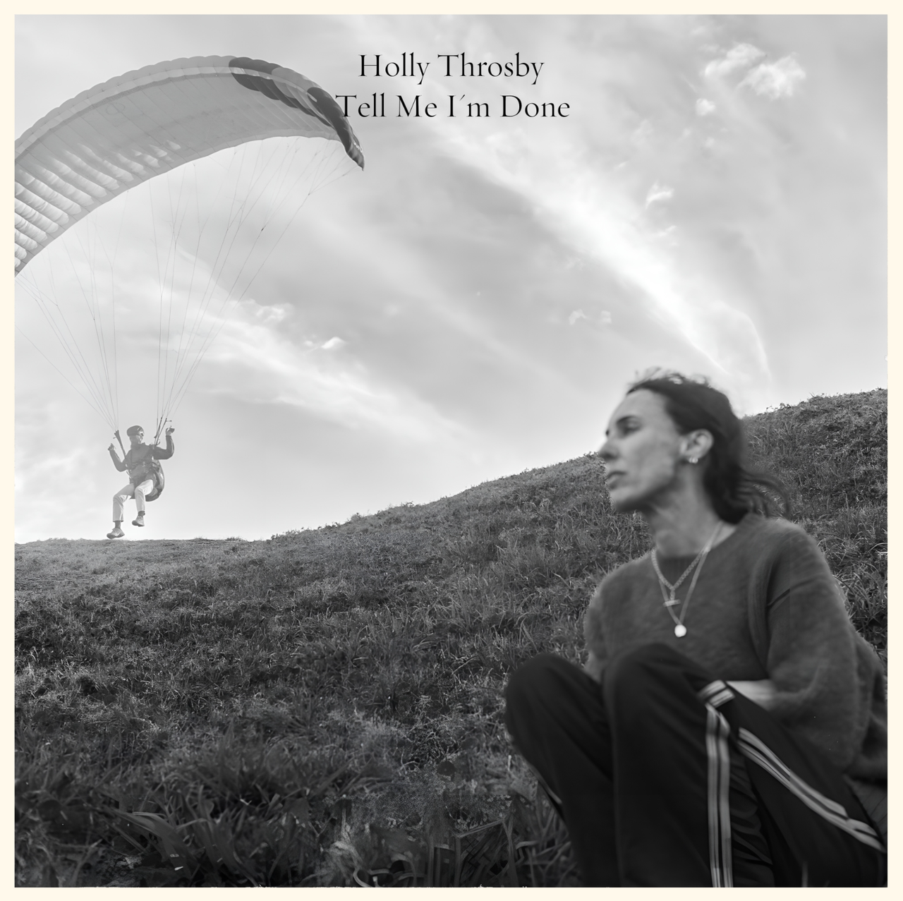 Black and white album cover for Holly Throsby's "Tell Me I'm Done" showing the artist on a grassy hill with a paraglider in the background.